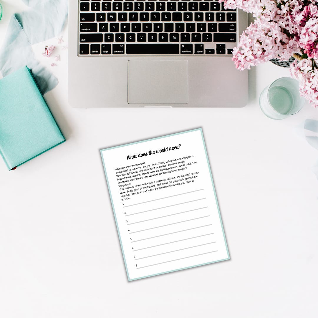 A laptop sits on a white desk next to vibrant flowers, a closed teal notebook, and a paper titled "What does the world need?" with lines encouraging contemplation. It's the ideal setup for jotting down ideas in your 'Find Your Purpose' Ebook & Workbook or drafting an inspiring ebook.
