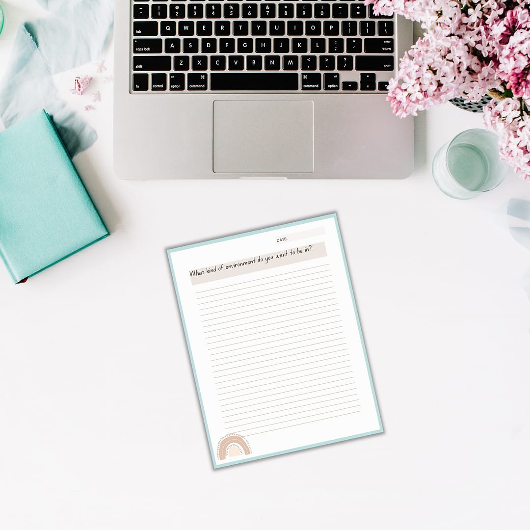 A laptop, open notebook, flowers, and a turquoise book are placed on a white desk. An empty 'Find Your Purpose' Journal with lined paper is titled "What kind of environment do you want to be in?