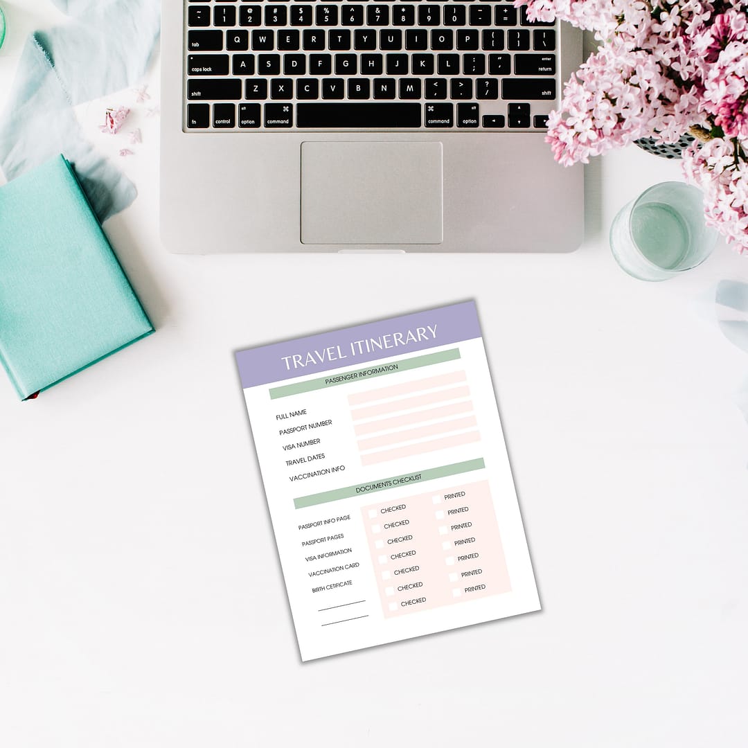 A laptop and flowers sit gracefully on a white desk, accompanied by The Dream Vacations Travel Planner, a notebook, and a pen, setting the stage for mapping out dream vacations.