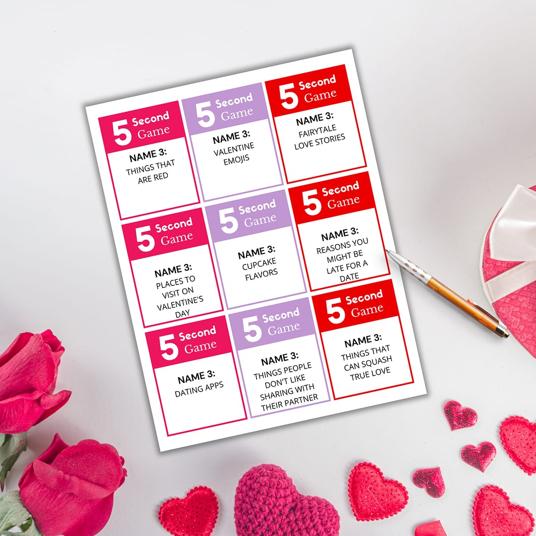 A "Valentine's 5-Second Game PLR" card lies on a white surface, surrounded by red and pink roses, a heart-shaped pen, and crocheted hearts, featuring Valentine-themed prompts to spark joy.