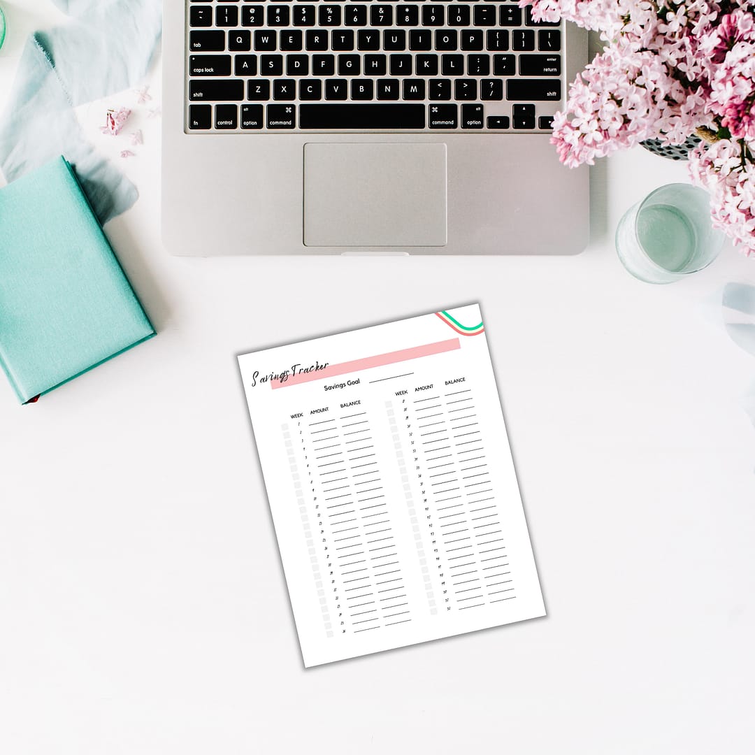 The 'New Year, New Start' Resolutions Planner pairs perfectly with a savings tracker sheet, positioned next to a laptop, turquoise book, and pink flowers on a white desk.