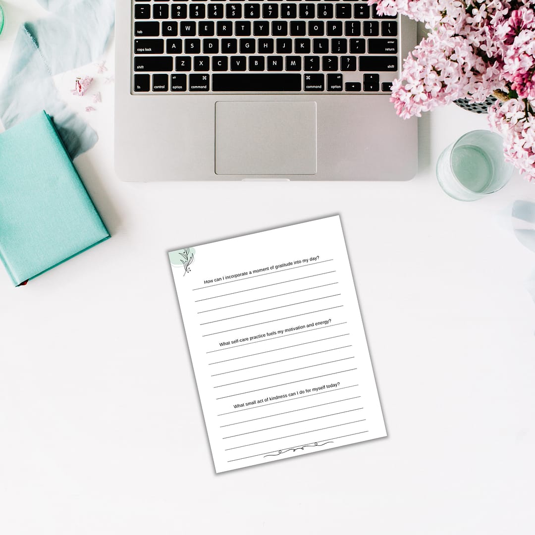 A laptop and a floral notebook are open on a desk, accompanied by a completed worksheet from The Power of Momentum Journal & Workbook. Pink flowers adorn the corner.